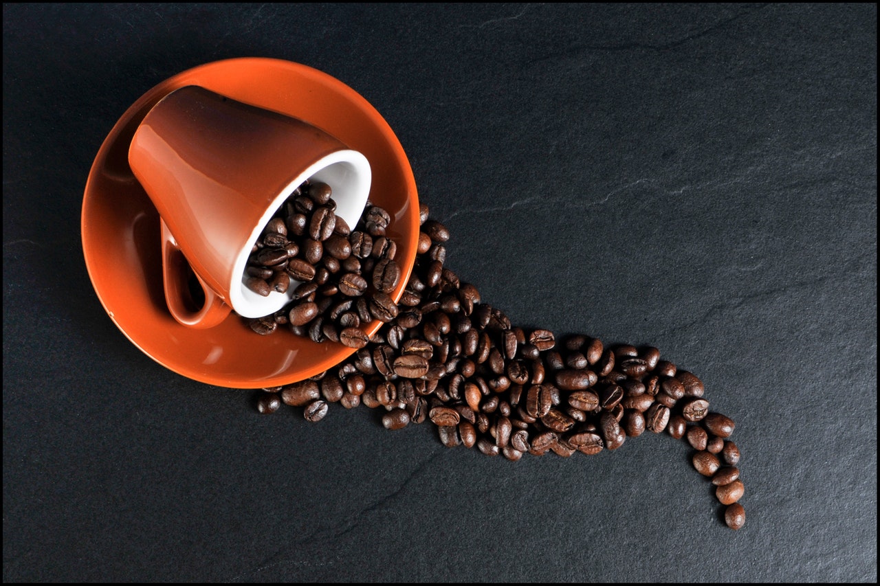 Coffee beans and ceramic mugs on black surface